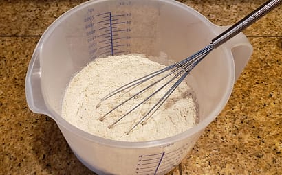 Dry ingredients for fiber-rich pancakes being stirred with a wire whisk in a plastic bowl.