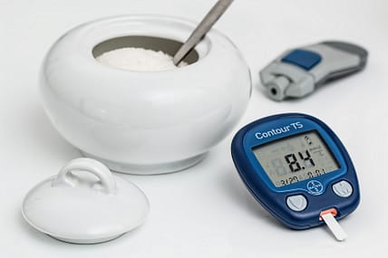 Diabetes represented by sugar in a bowl along with a glucose meter