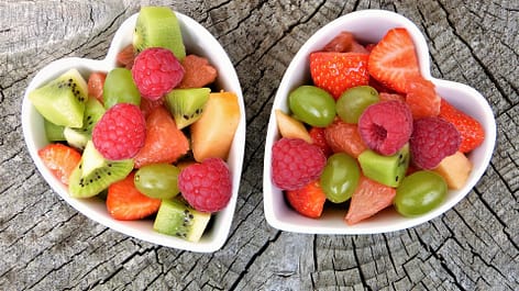 Two heart shaped bowls with a variety of fruit for dessert instead of sweets. Fruit is part of a healthy South Asian diet