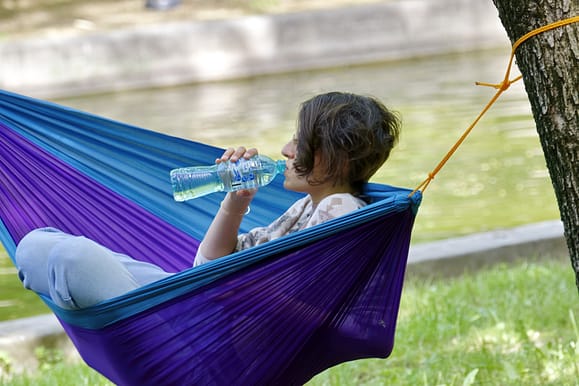 Woman in a hammock drinking water from a bottle to hydrate.
