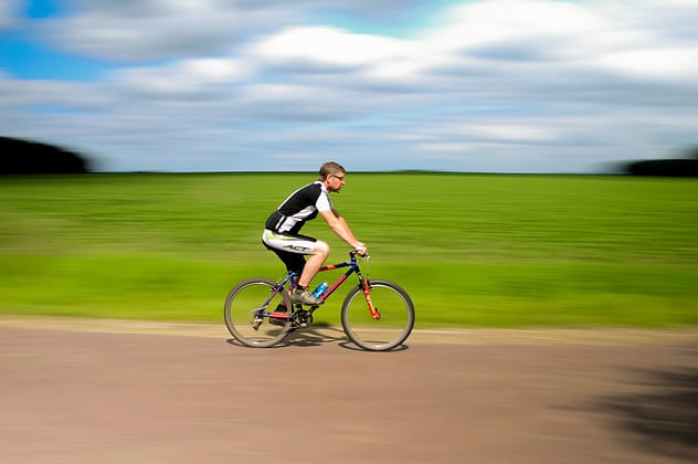 Man riding his bicycle on a road. This fulfills the exercise recommendation of moderate-vigorous aerobic exercise.
